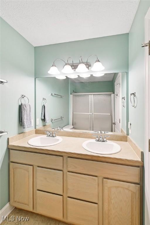 full bathroom featuring double vanity, a sink, a textured ceiling, and a shower stall