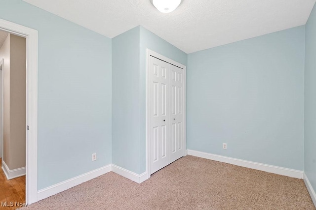 unfurnished bedroom featuring baseboards, a closet, a textured ceiling, and light colored carpet