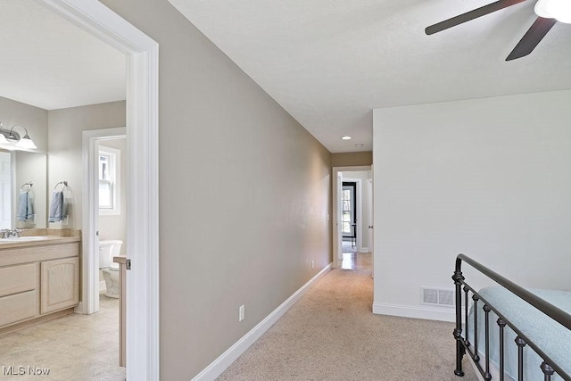 hallway with visible vents, light carpet, baseboards, a sink, and an upstairs landing