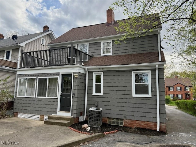 rear view of property featuring a chimney, roof with shingles, central AC, a balcony, and entry steps