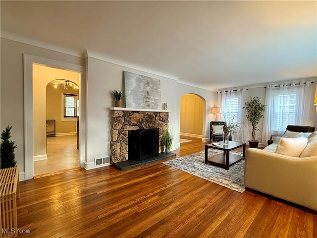 living room featuring a fireplace, arched walkways, baseboards, wood finished floors, and visible vents