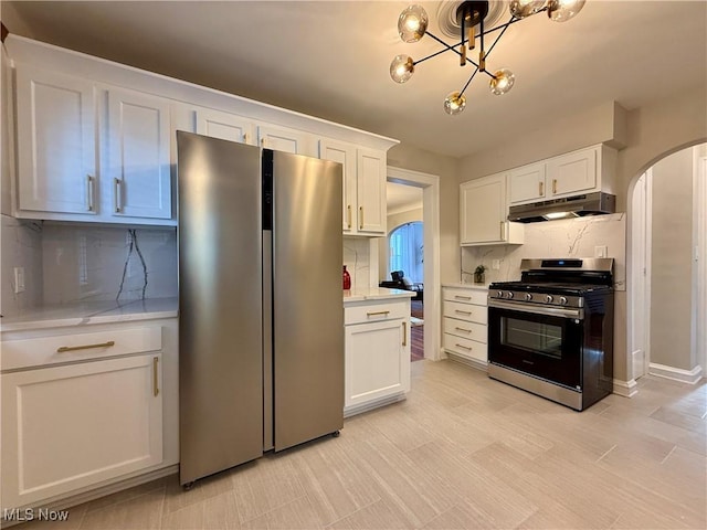 kitchen with white cabinets, appliances with stainless steel finishes, arched walkways, decorative backsplash, and under cabinet range hood