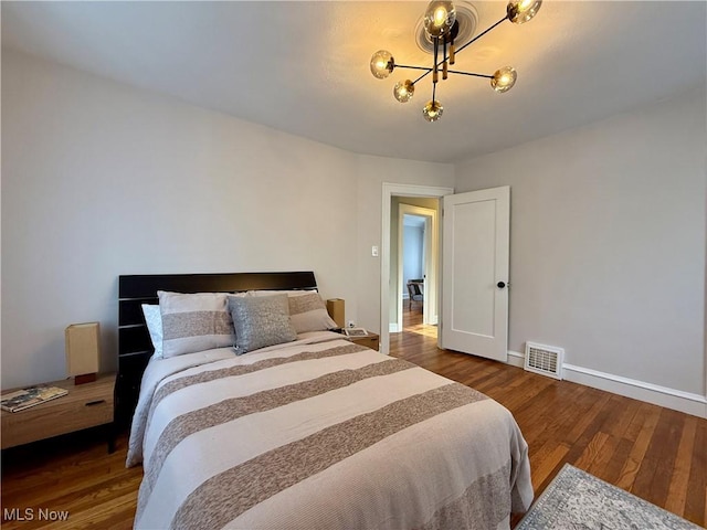 bedroom featuring wood finished floors, baseboards, a chandelier, and visible vents