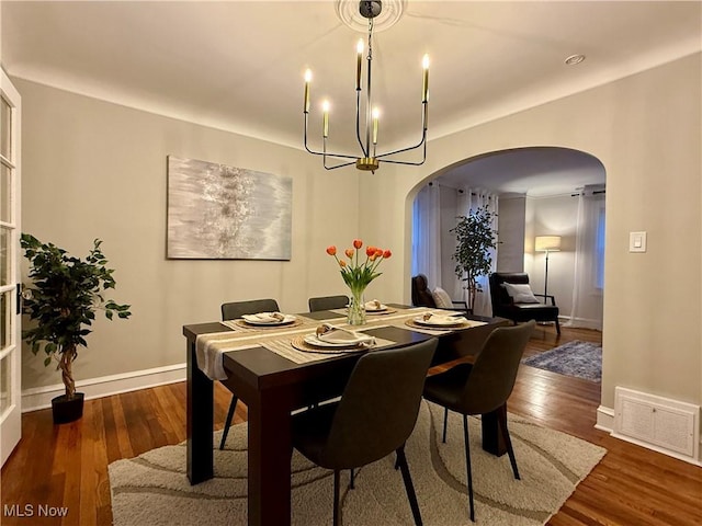 dining space with visible vents, wood finished floors, baseboards, a chandelier, and arched walkways