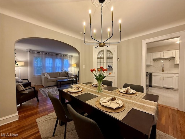 dining space featuring light wood-type flooring, arched walkways, and a notable chandelier