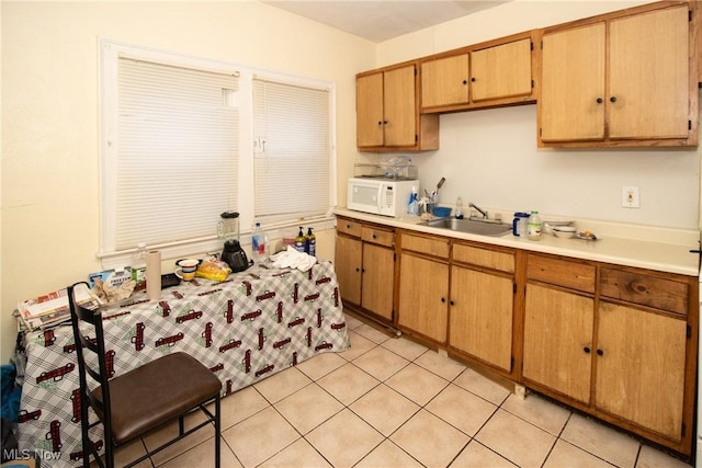 kitchen with a sink, light tile patterned floors, white microwave, and light countertops