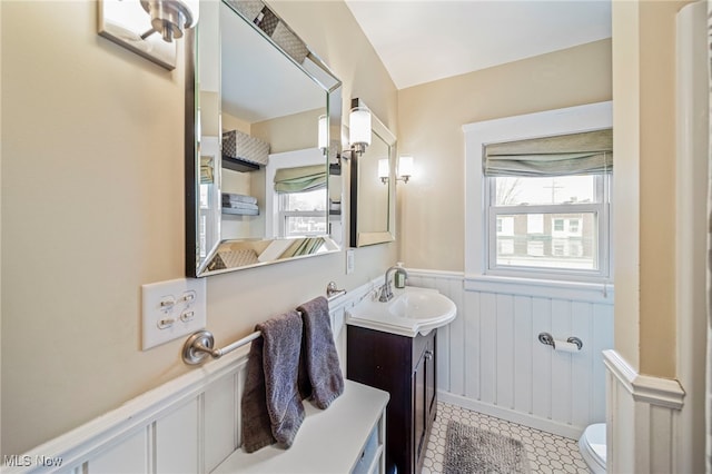 bathroom featuring vanity, a decorative wall, toilet, tile patterned floors, and a wainscoted wall