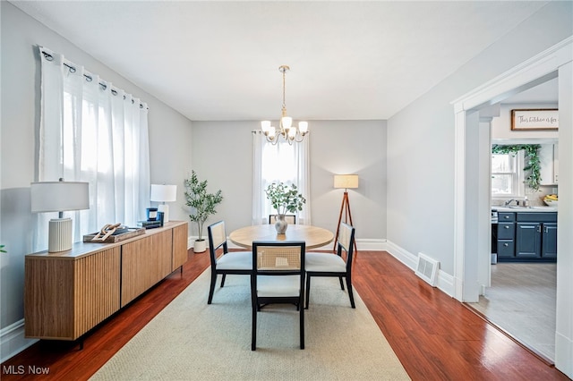 dining area with dark wood-style flooring, baseboards, visible vents, and an inviting chandelier