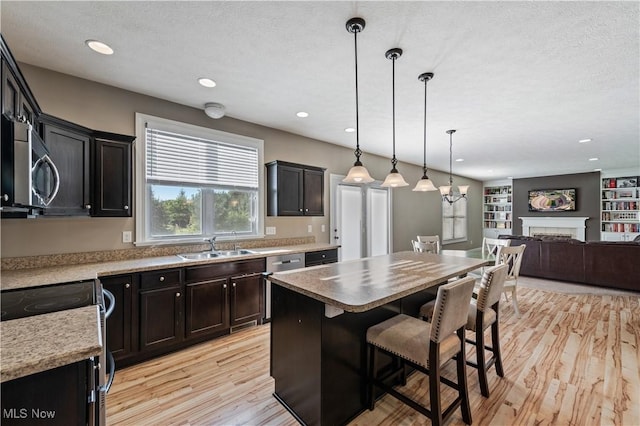 kitchen featuring a sink, a fireplace, light wood-style flooring, stainless steel appliances, and open floor plan