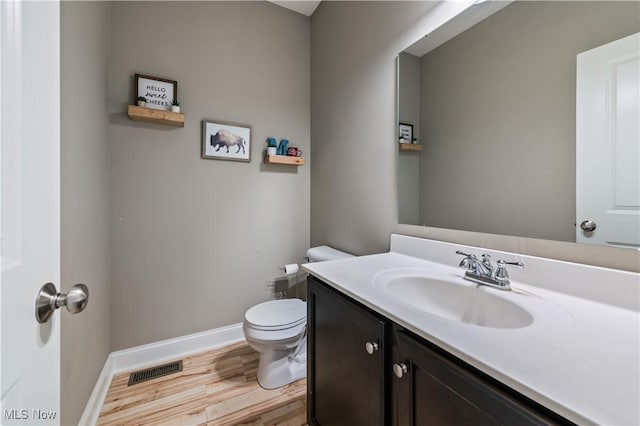 half bath featuring visible vents, vanity, wood finished floors, toilet, and baseboards