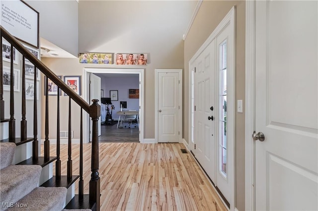 foyer entrance featuring stairway, baseboards, light wood-type flooring, and lofted ceiling