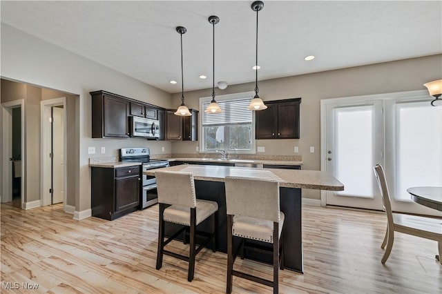 kitchen with dark brown cabinetry, light countertops, stainless steel appliances, light wood-type flooring, and a kitchen island