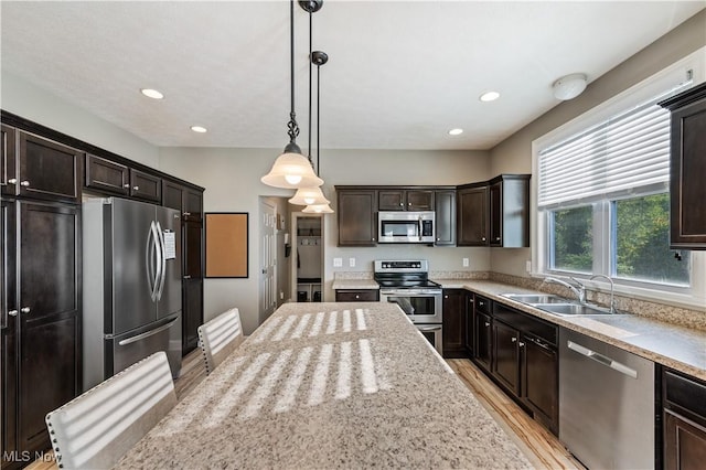 kitchen with dark brown cabinets, light wood-style floors, a sink, hanging light fixtures, and stainless steel appliances