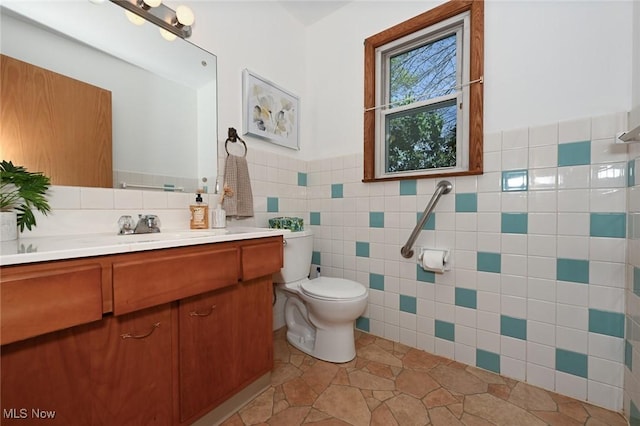 bathroom featuring vanity, wainscoting, toilet, and tile walls