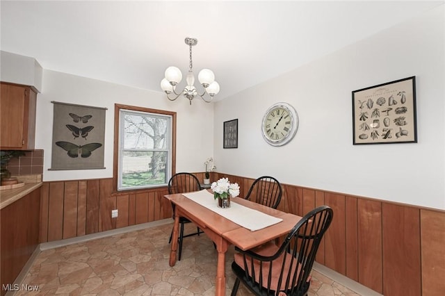 dining space with an inviting chandelier, wood walls, and a wainscoted wall