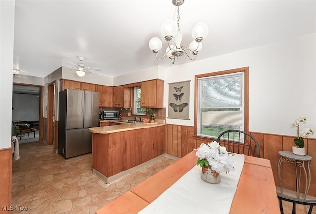 kitchen with wood walls, a peninsula, light countertops, a wainscoted wall, and appliances with stainless steel finishes