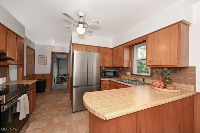 kitchen with a sink, light countertops, stainless steel appliances, a peninsula, and under cabinet range hood