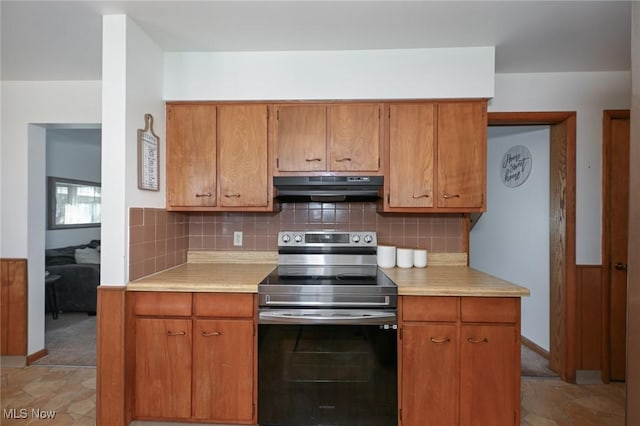 kitchen with brown cabinetry, light countertops, under cabinet range hood, stainless steel electric stove, and backsplash