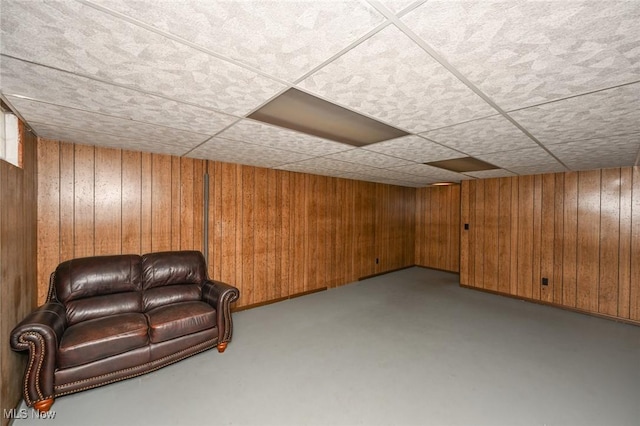 unfurnished room with wooden walls, a drop ceiling, and finished concrete floors