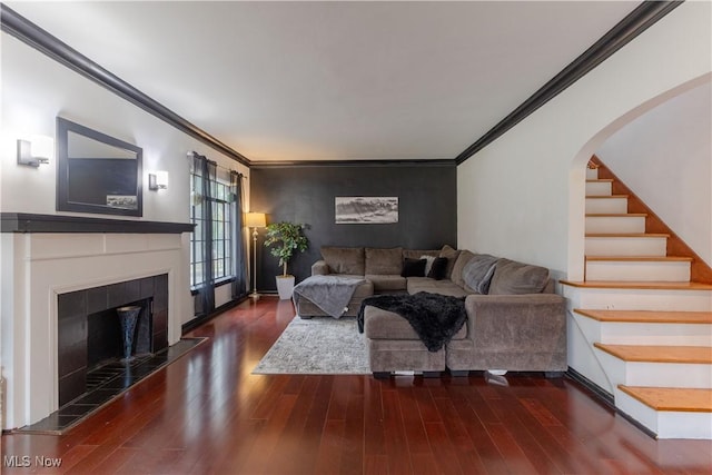 living room with crown molding, a tiled fireplace, and wood finished floors