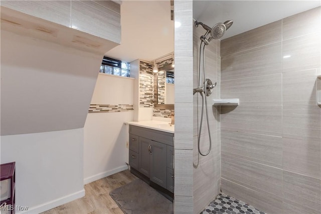 full bath featuring vanity, backsplash, a tile shower, and wood finished floors