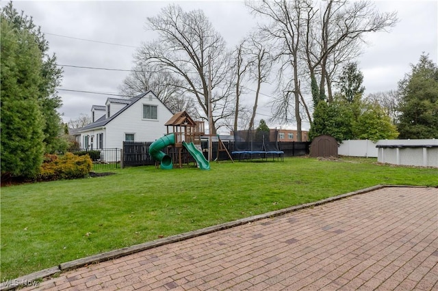 view of playground with a yard, a fenced backyard, a trampoline, and a storage unit