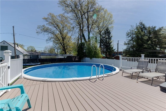 view of pool with a fenced in pool, a wooden deck, a fenced backyard, and a trampoline