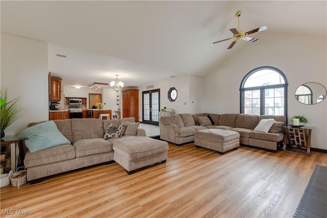 living area with light wood-type flooring, ceiling fan with notable chandelier, and high vaulted ceiling
