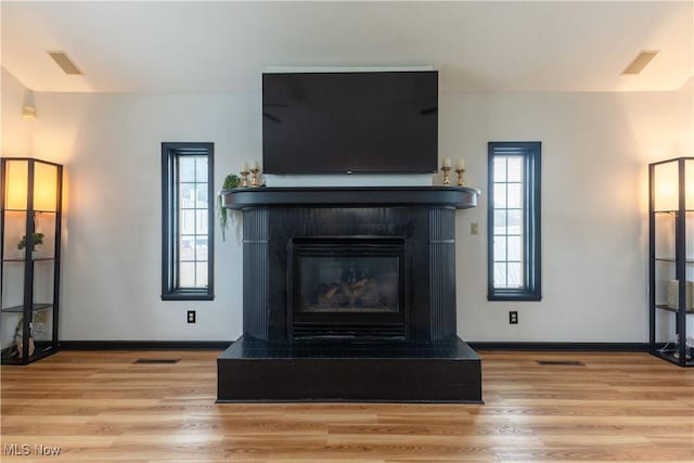 details featuring visible vents, baseboards, a glass covered fireplace, and wood finished floors