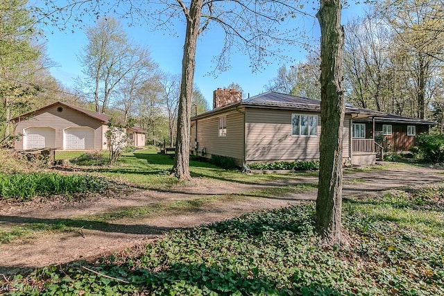 view of side of home featuring an outdoor structure, a garage, a chimney, metal roof, and a yard