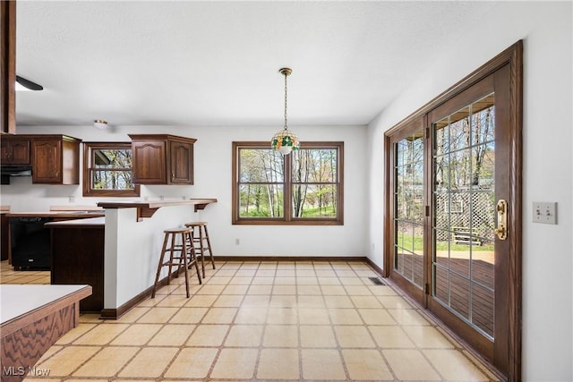 kitchen with pendant lighting, a peninsula, a breakfast bar, baseboards, and under cabinet range hood