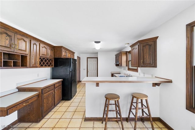 kitchen featuring a kitchen bar, a sink, freestanding refrigerator, a peninsula, and light floors