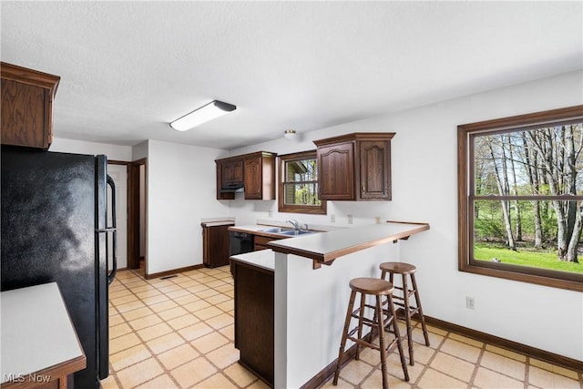 kitchen with baseboards, a sink, black appliances, and a kitchen bar