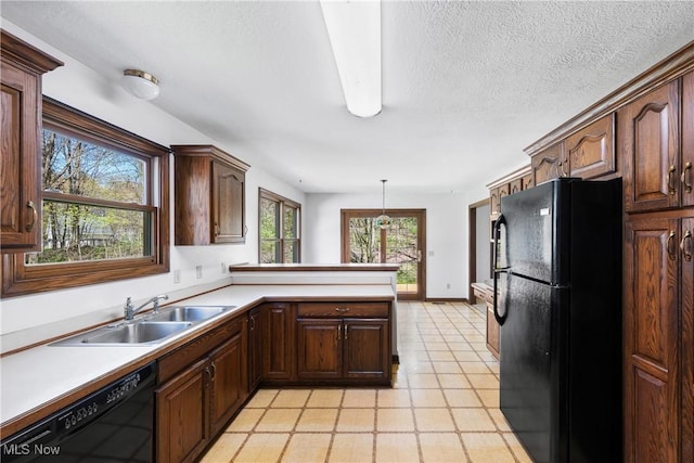 kitchen with pendant lighting, a sink, light countertops, black appliances, and a peninsula