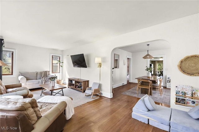 living room with arched walkways, plenty of natural light, baseboards, and hardwood / wood-style flooring
