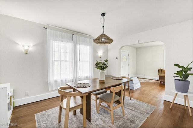 dining room featuring arched walkways, baseboards, and hardwood / wood-style floors