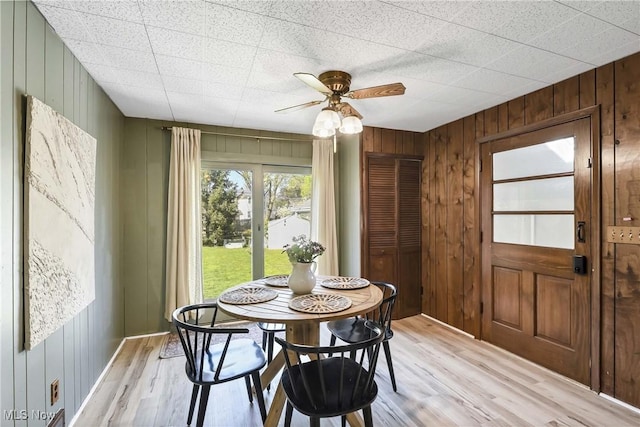 dining room with wooden walls, a ceiling fan, and light wood-style flooring