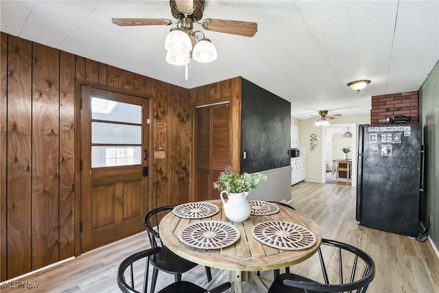 dining room with light wood finished floors, ceiling fan, and wooden walls