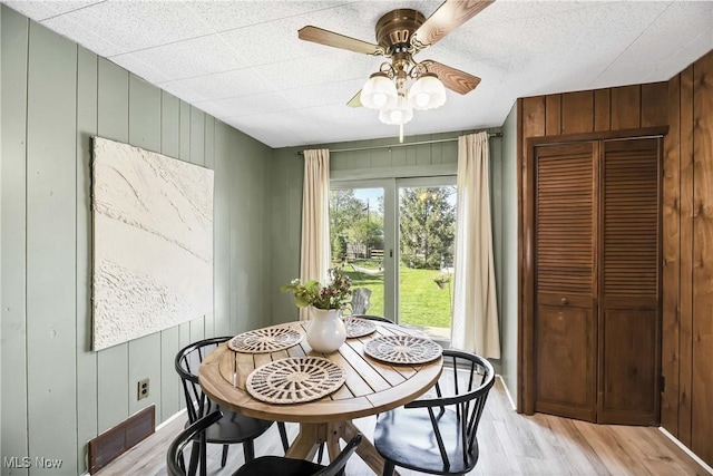 dining room with light wood-style floors, ceiling fan, wooden walls, and visible vents