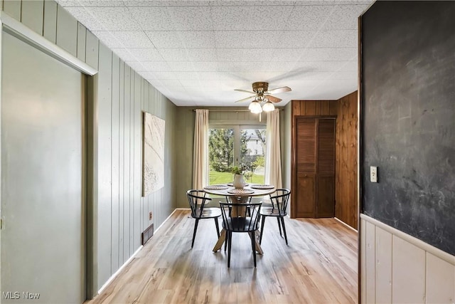 dining area with ceiling fan, wood walls, light wood-style flooring, and visible vents