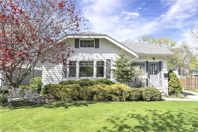 view of front of property with roof with shingles, fence, and a front yard
