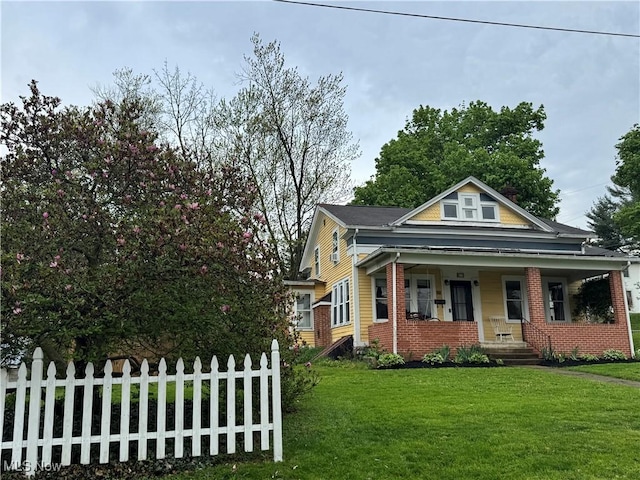 bungalow-style house featuring brick siding, fence, covered porch, and a front yard