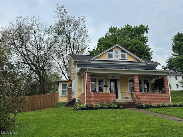 bungalow-style home featuring brick siding, a front lawn, fence, and covered porch