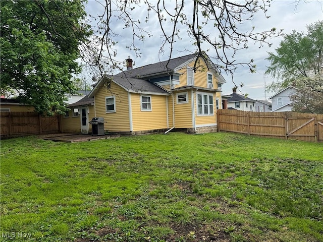 back of house featuring a lawn, a chimney, and a fenced backyard