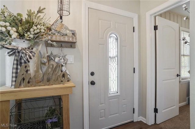 foyer entrance with baseboards, dark carpet, and a wealth of natural light