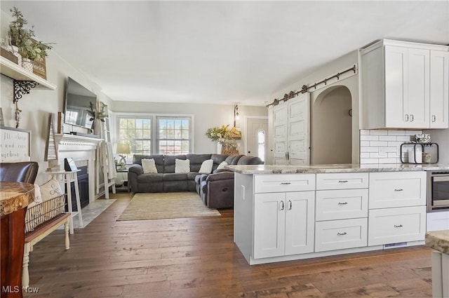 kitchen featuring backsplash, light stone counters, a peninsula, white cabinetry, and dark wood-type flooring
