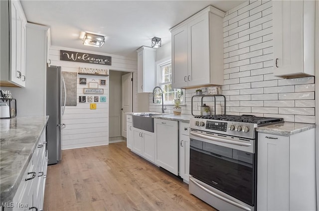 kitchen with appliances with stainless steel finishes, a sink, light wood-style flooring, white cabinetry, and decorative backsplash