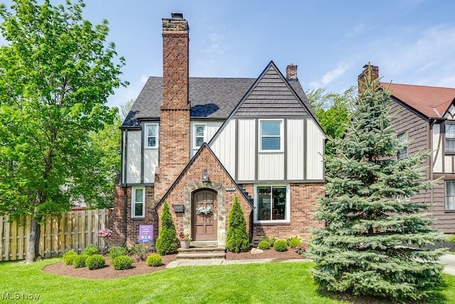view of front of property with board and batten siding, a chimney, brick siding, fence, and a front lawn