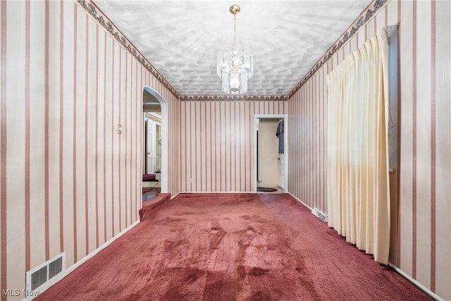 carpeted empty room featuring an inviting chandelier, arched walkways, wallpapered walls, and visible vents