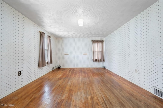 unfurnished room with wallpapered walls, visible vents, baseboards, and hardwood / wood-style floors
